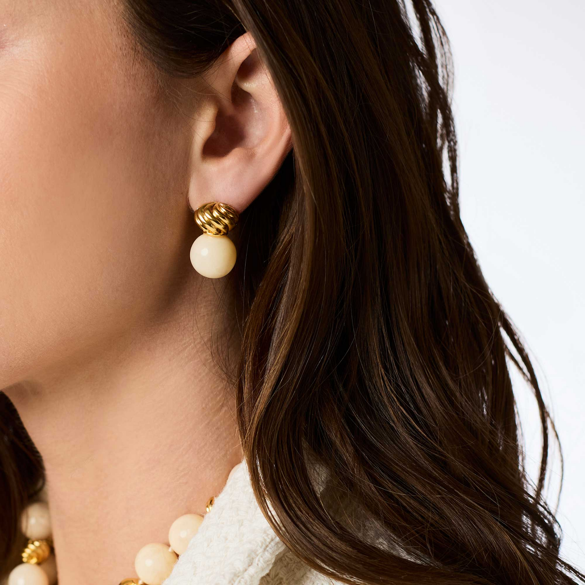 Woman wearing a Ravello Midi Earring featuring a gold twisted stud and a cream resin bead.