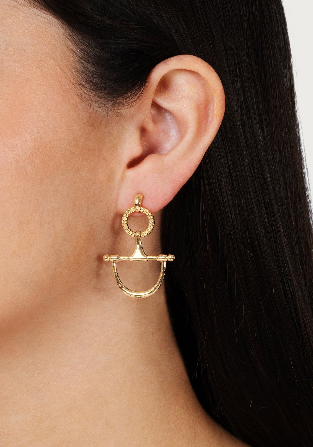 Close-up of a person wearing a gold Cheval Bit drop earring with a braided ring and bit design.