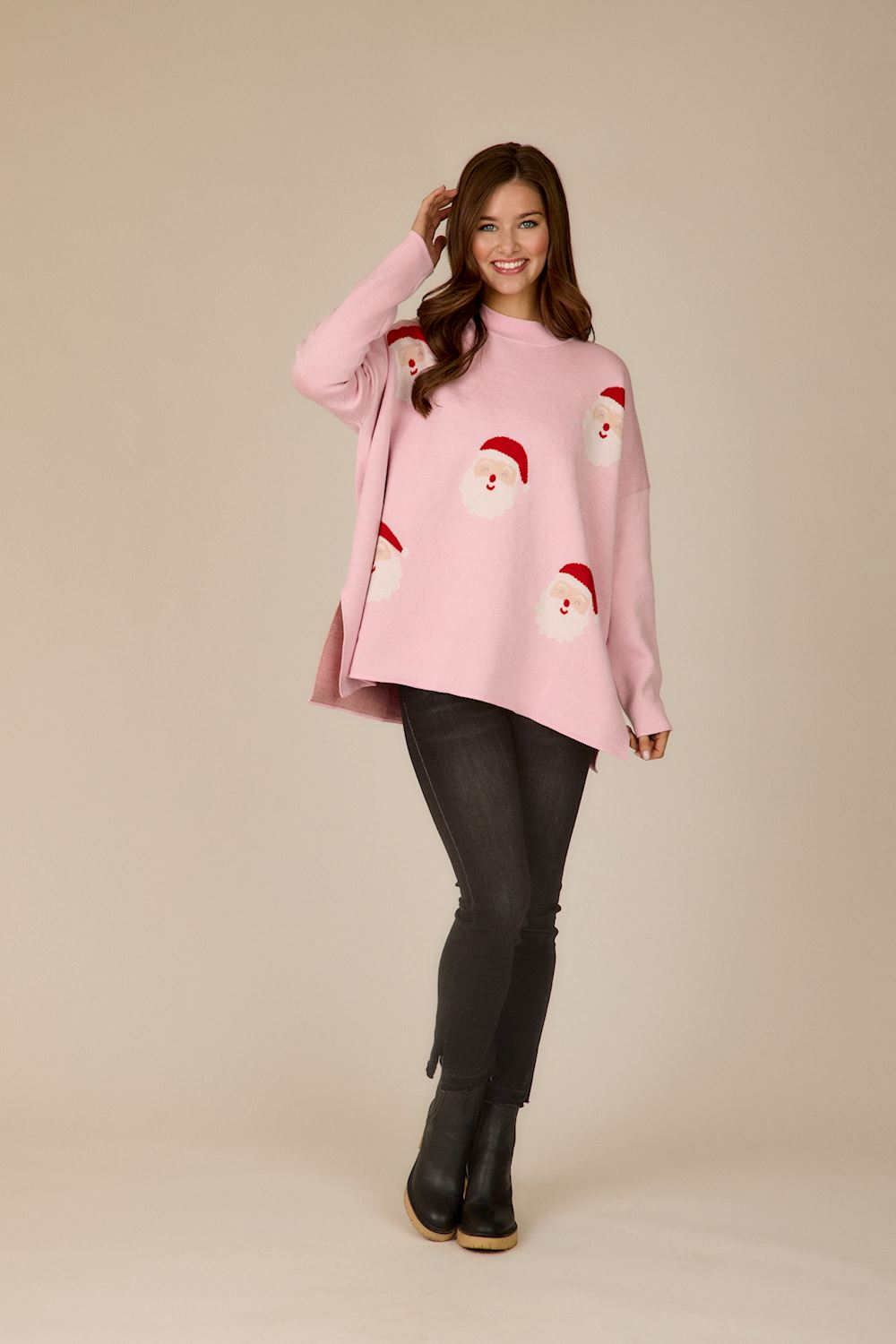 Woman wearing a pink Holiday Jacquard Sweater with Santa Claus patterns and black skinny jeans.