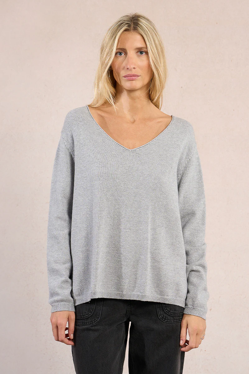 Woman wearing a light grey V-neck Lesli knitted sweater with long sleeves and black pants.