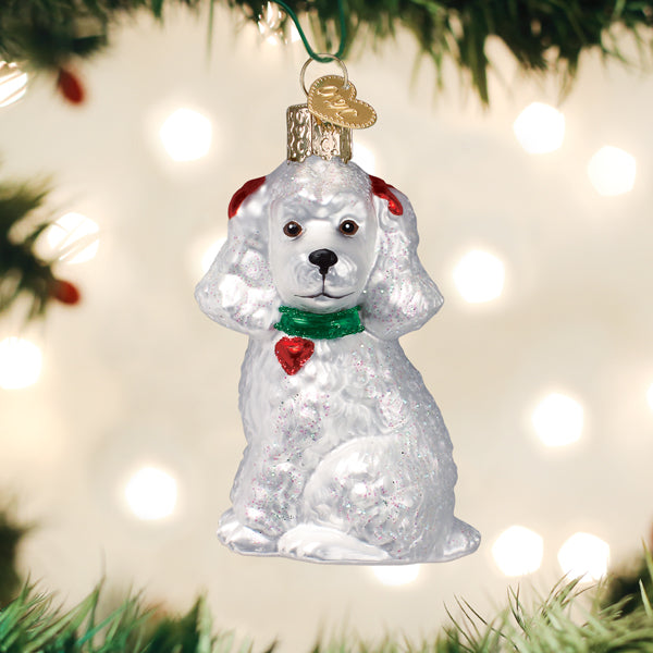 White Poodle glass ornament with a green collar and red heart charm on a Christmas tree.
