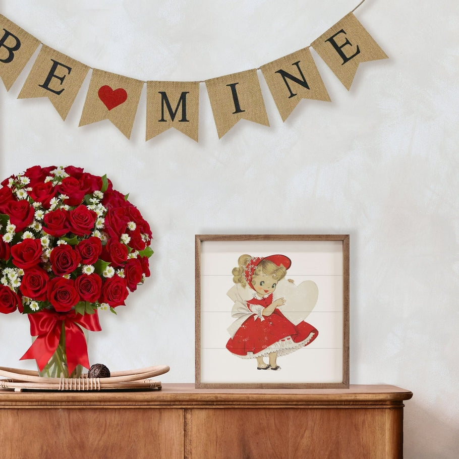 Vintage Valentine Girl with Heart framed wood art on a wooden sideboard next to red roses.