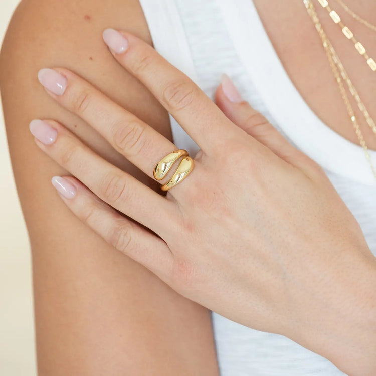 A person wearing an 18k gold plated adjustable wrap ring on their middle finger.