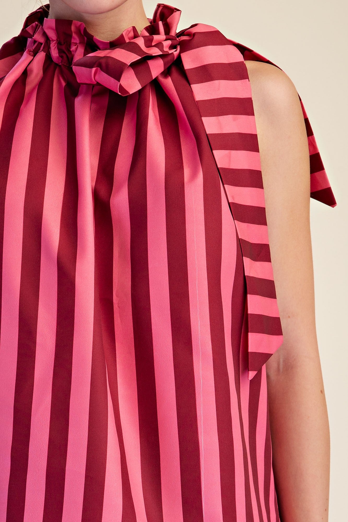 Close-up of a pink and burgundy vertical stripe sleeveless top with a ruffled tie neckline.