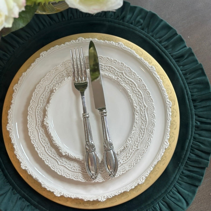 Round dark green velvet placemat with a ruffled edge, featuring a layered white and gold table setting.