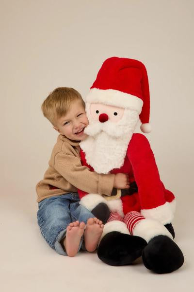 A young boy sitting on the floor hugging a large, soft Santa Claus plush toy.