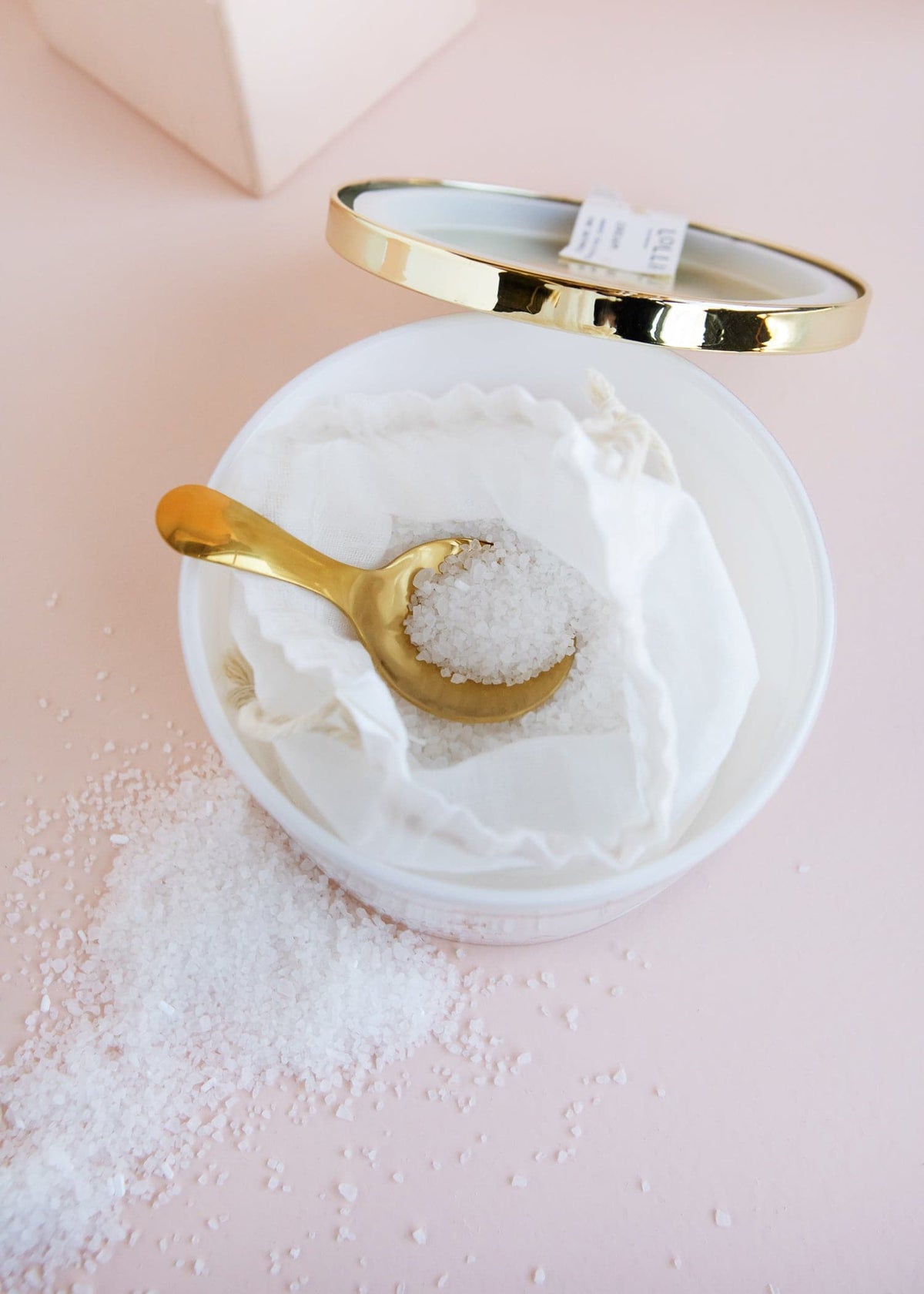 White glass jar with gold accents holding sea salt in a linen bag