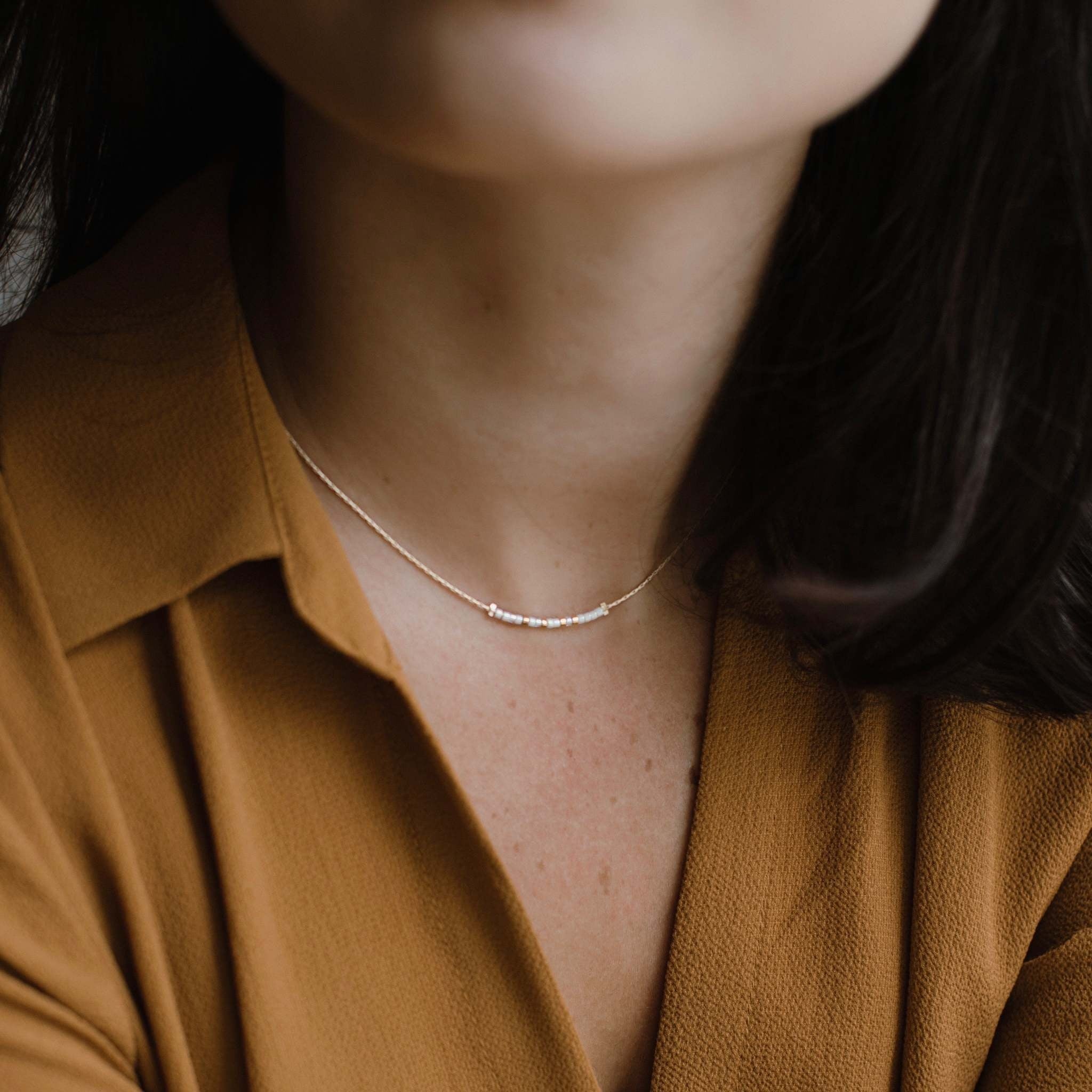 Faith necklace featuring iridescent pearl beads with shimmering cream gold accents in a neutral pattern.