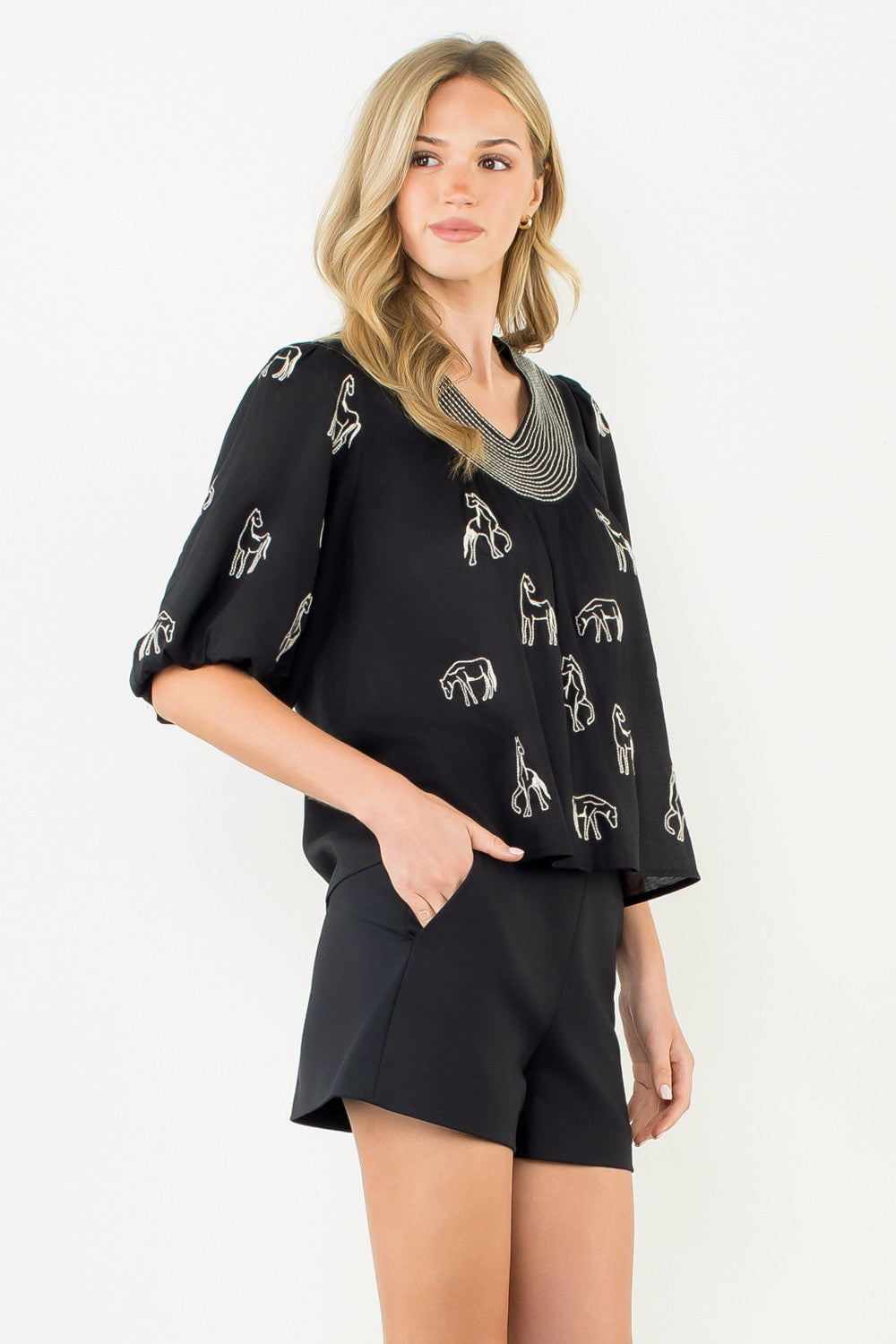 Woman wearing the Abigail black top with white horse embroidery and puff sleeves.
