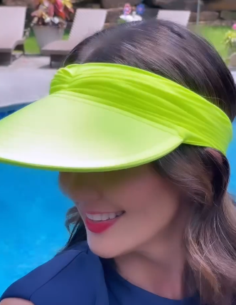 Woman wearing a neon lime green ruched stretchy headband sun visor hat by a swimming pool.