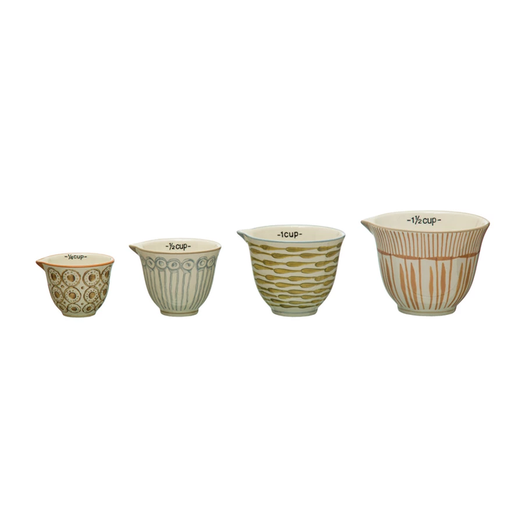 Set of four stoneware measuring cups with colorful geometric patterns on a white background.