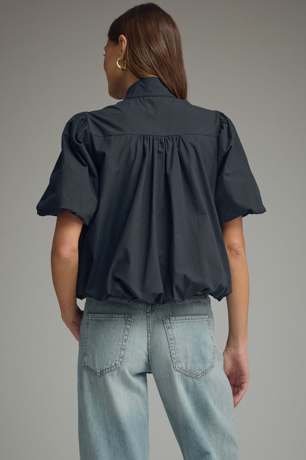 Back view of a woman wearing a black Jacky short puff sleeve top with a bubble hem and light jeans.