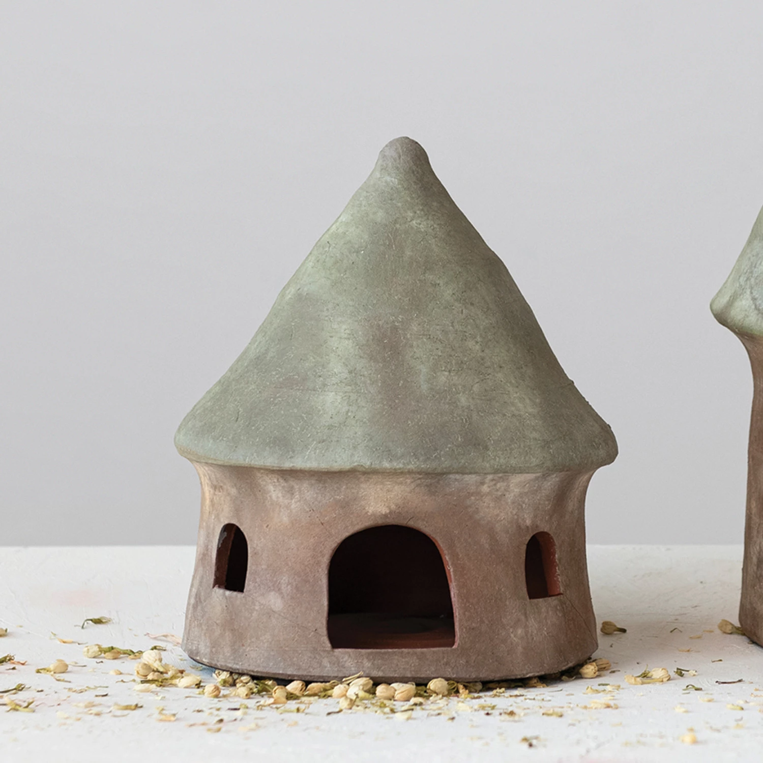 Terra-cotta toad house with a green conical roof and natural brown base with arched openings.