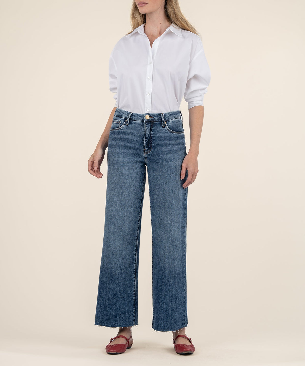 Woman wearing Meg high rise wide leg jeans in medium wash with a raw hem and white button-down shirt.