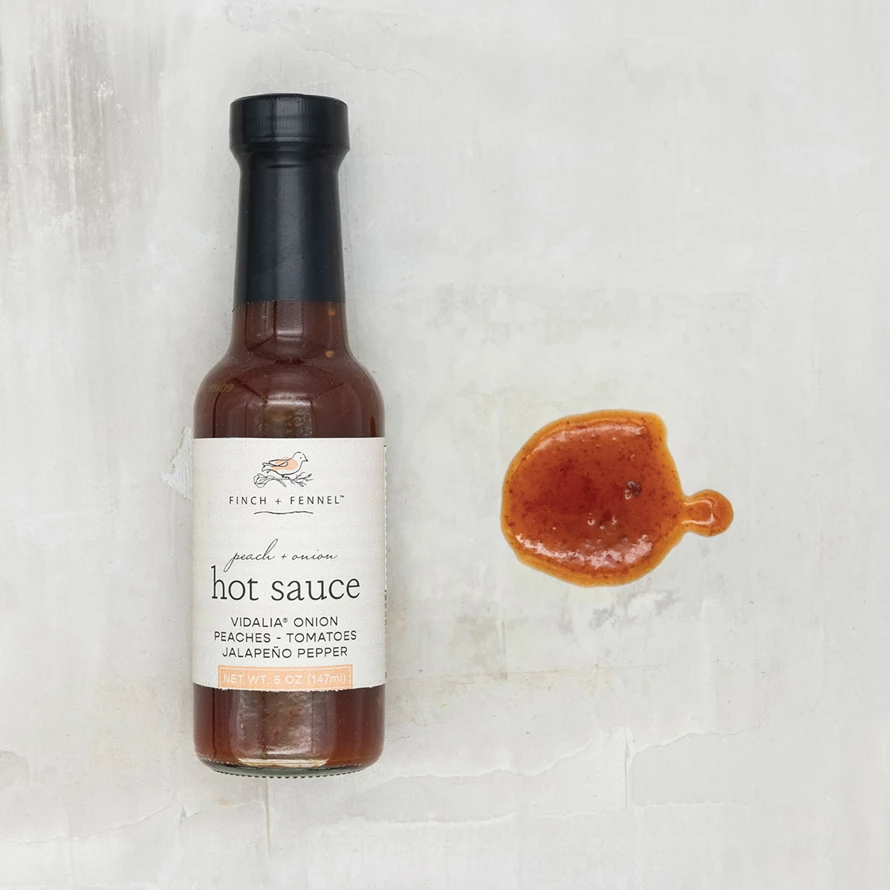 Bottle of Peach + Onion Hot Sauce with a peach-colored label.