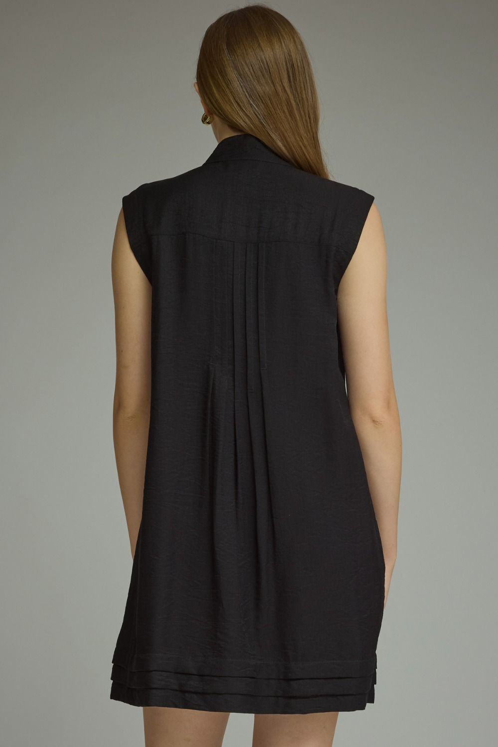 Back view of a woman wearing a black sleeveless Thea mini dress with pleated back detail.