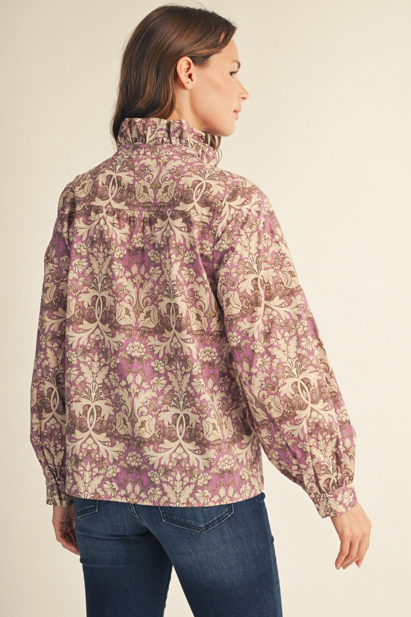 Back view of a woman wearing a purple baroque floral blouse with a ruffled collar and long sleeves.