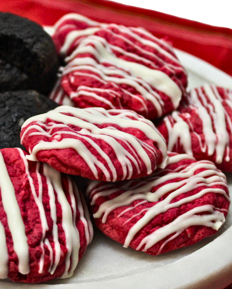 Red velvet soft batch cookies with white icing drizzle on a white plate.