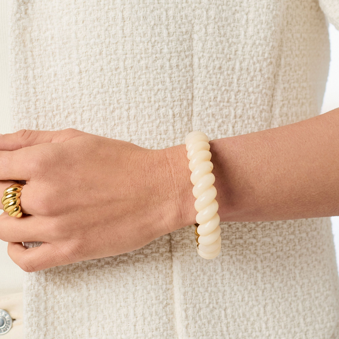 A person wearing the Ravello Statement Bangle, a cream-colored twisted resin bracelet.