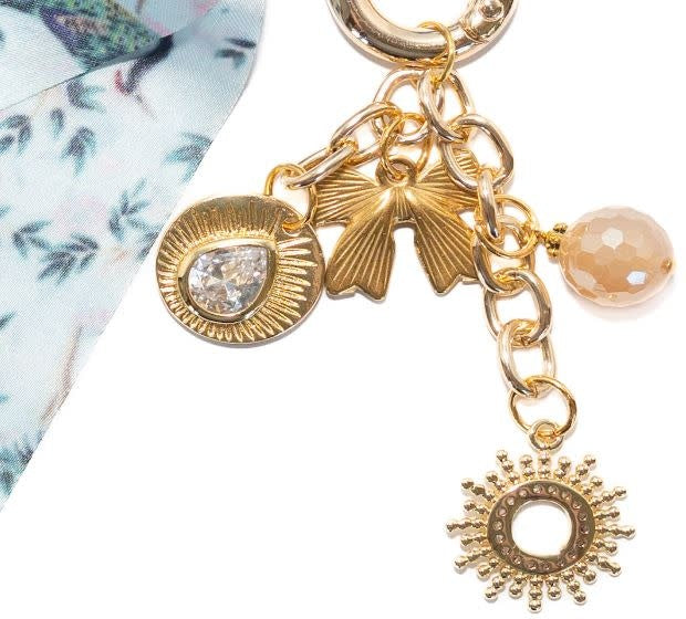 Peacock Paradise bag charm featuring iridescent blue-green peacock feather pattern on a gold-tone metal silhouette.