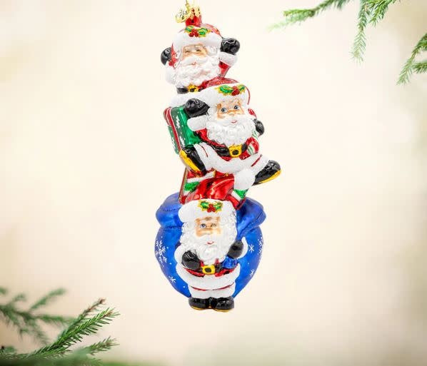 Three mischievous Santa figurines with festive hats holding a gift bag