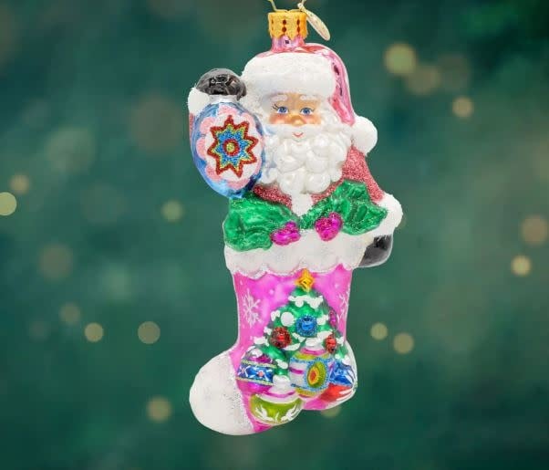 Santa figurine in shimmering suit with glittery hat holding colorful shiny ornaments