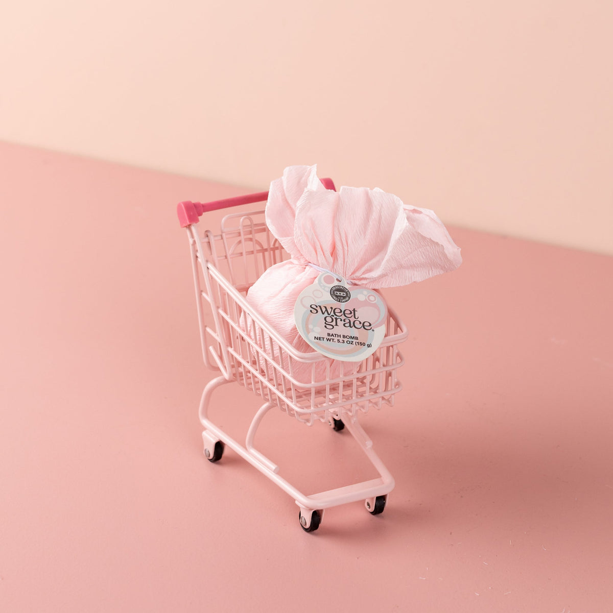 Sweet Grace Bath Bomb wrapped in pink paper inside a miniature pink shopping cart.