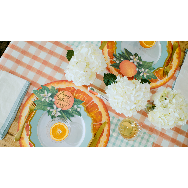 A table set with a peach and white painted check runner, orange-themed plates, and white hydrangeas.