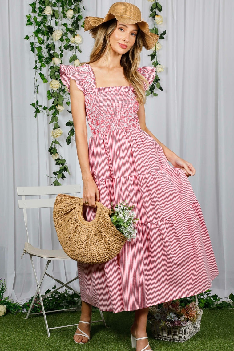 Woman wearing the Angela red and white striped tiered midi dress with a straw hat and bag.