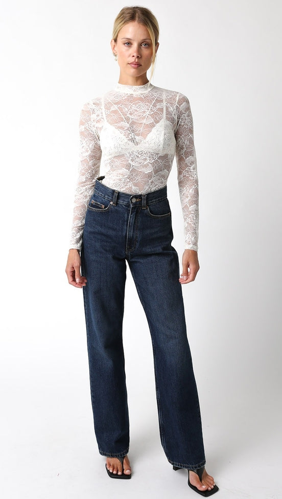 White lace long-sleeve mock neck top with a floral pattern, worn with dark wash wide-leg jeans.