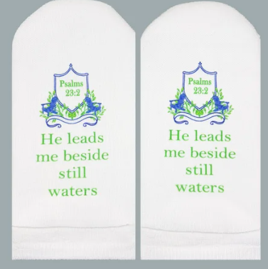 White socks featuring a blue crest and green text reading "He leads me beside still waters".