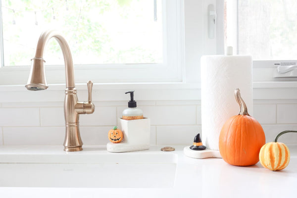 White ceramic soap dispenser with a small jack-o'-lantern decoration and a striped gourd.