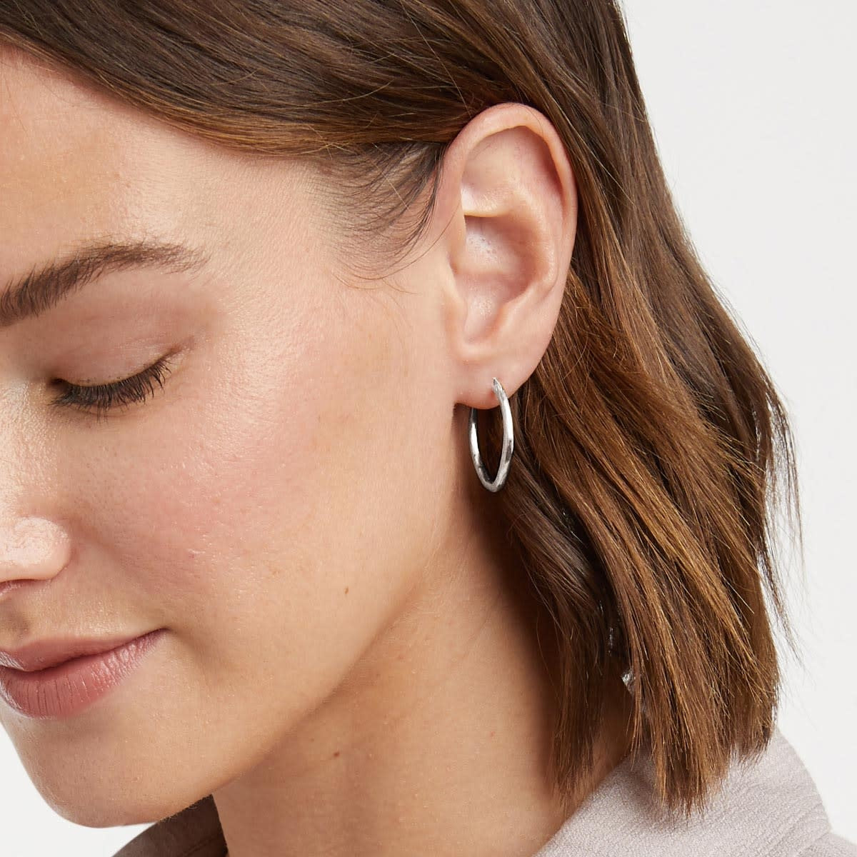 Silver fleur-de-lis hoop earring with hammered texture worn as a single piece.