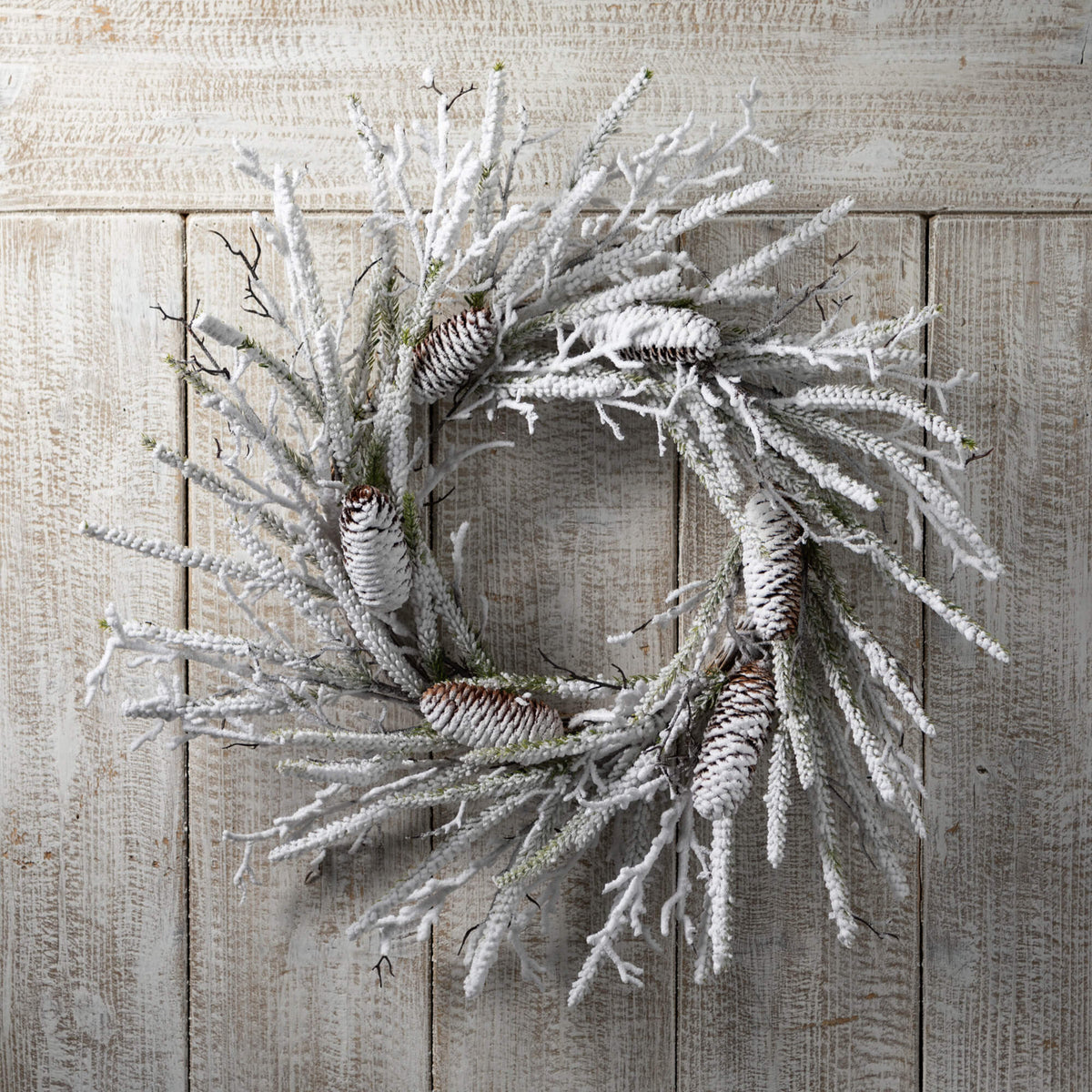 Flocked pine twig wreath with faux snow coating in neutral tones.