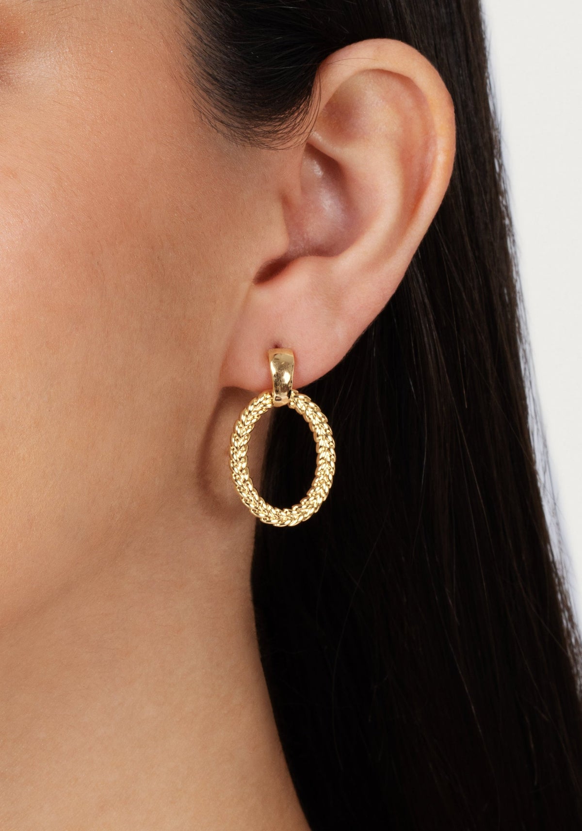 Close-up of a woman wearing a gold Cheval Ring Earring with a braided texture.