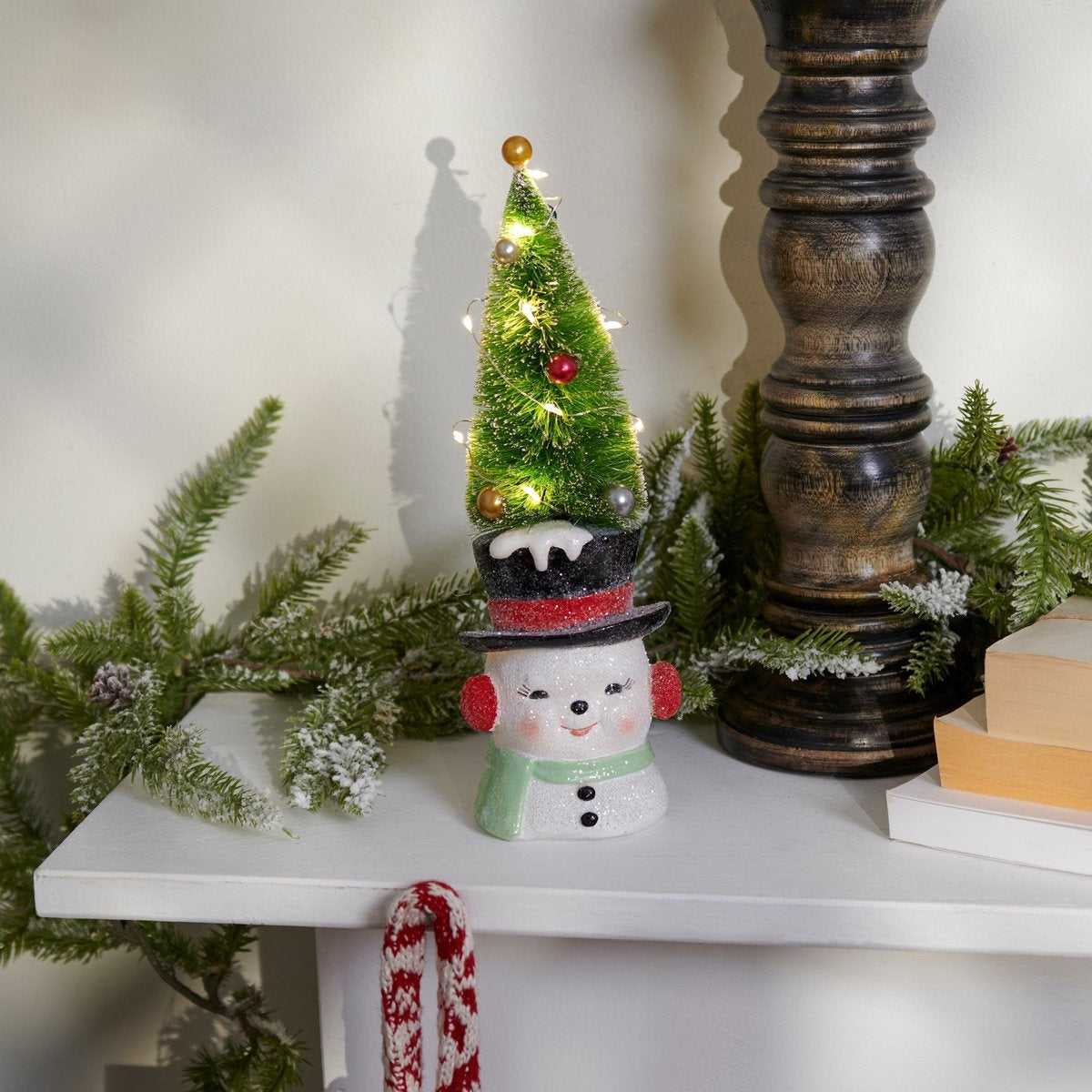 Lighted snowman figurine wearing a top hat with a green bottle brush Christmas tree on top.