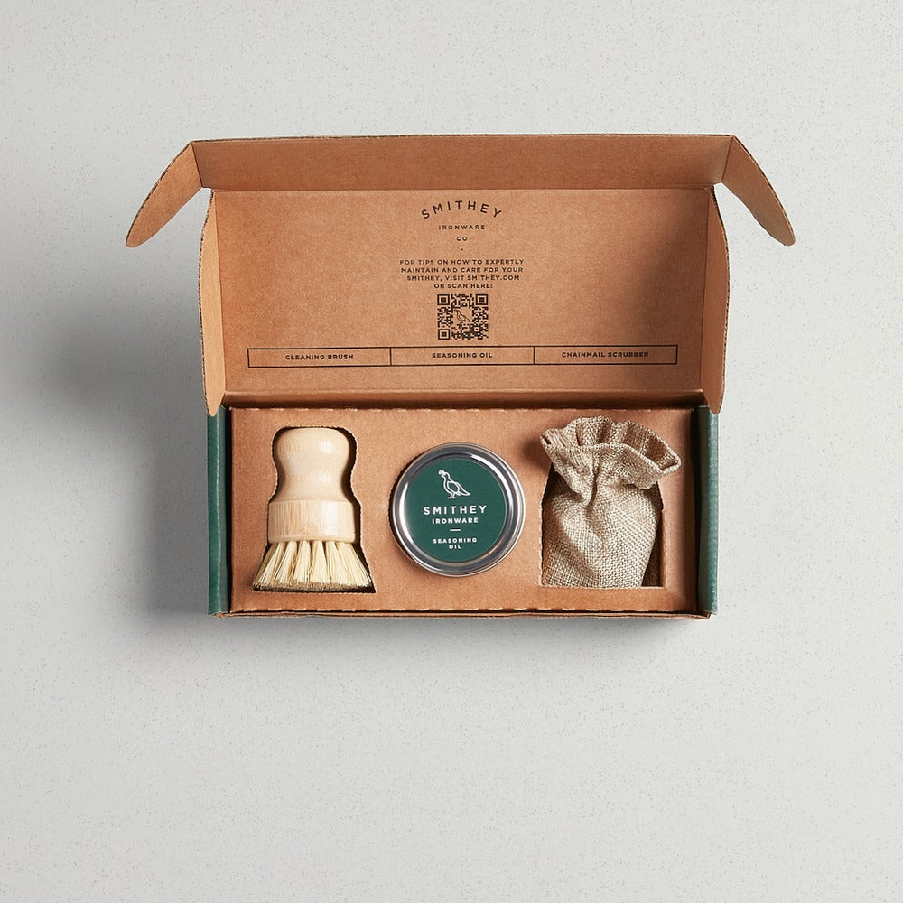 Smithey Ironware Cleaning & Care Kit with a wooden brush, seasoning oil, and chainmail scrubber.