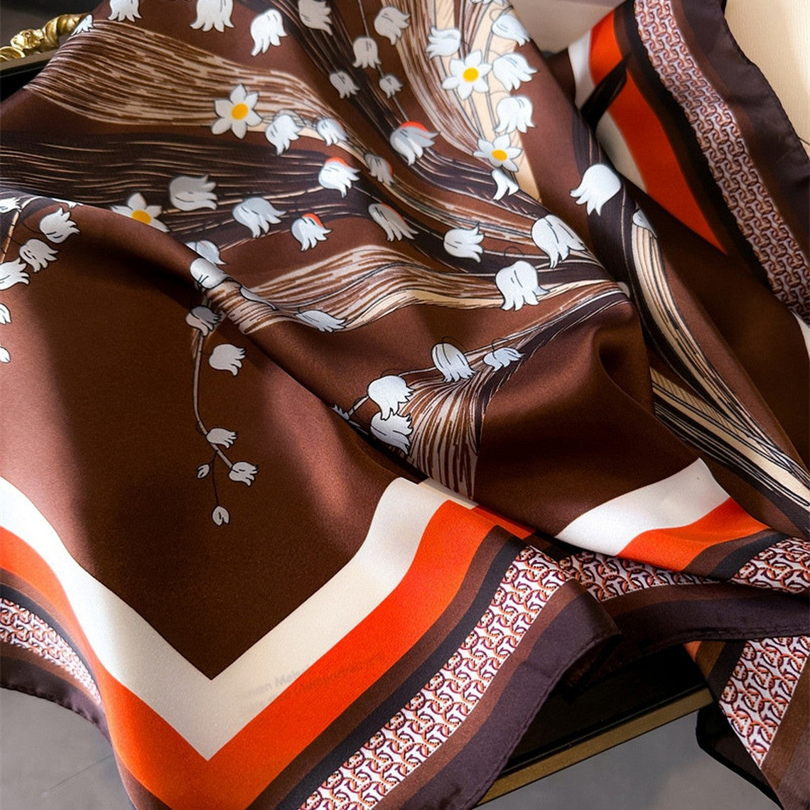 Artistic printed small square scarf in brown with white floral patterns and orange border stripes.