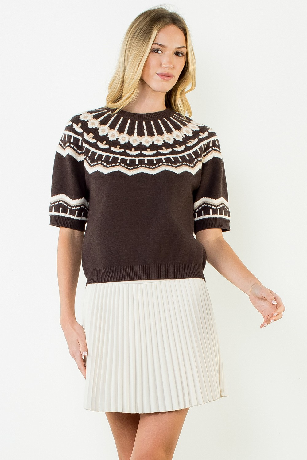 Woman wearing the Nicole Short Sleeve Pattern Sweater in brown with a white pleated skirt.