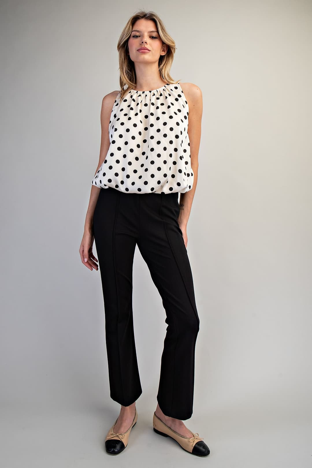 Woman wearing the Monique Polka Dot Sleeveless Blouse with black pants and beige flats.