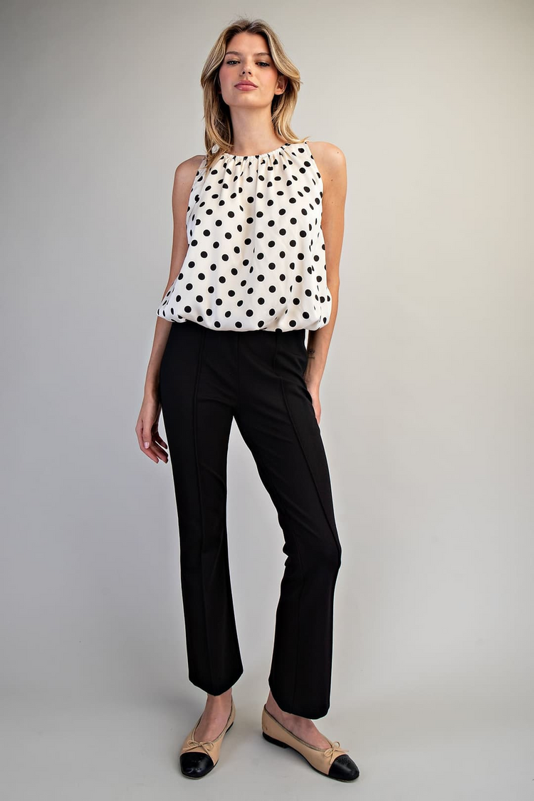 Woman wearing the Monique Polka Dot Sleeveless Blouse with black pants and beige flats.