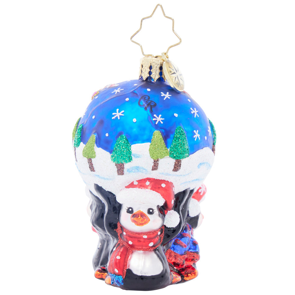 Glass penguin ornament wearing a Santa hat and scarf, holding up a snowy blue globe with trees.