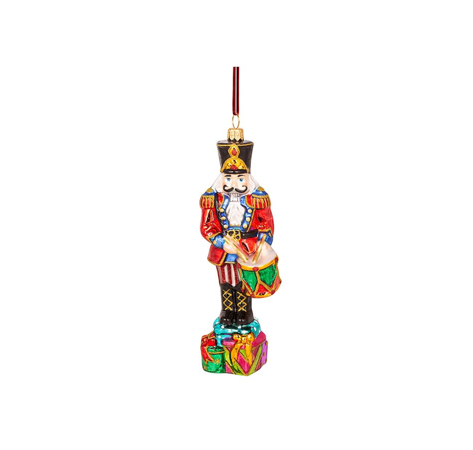 Hand-crafted blown glass Viennese Nutcracker ornament playing a drum atop a stack of gifts.