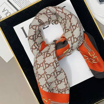Luxury chain print velvet scarf in orange and brown with a repeating monogram pattern.