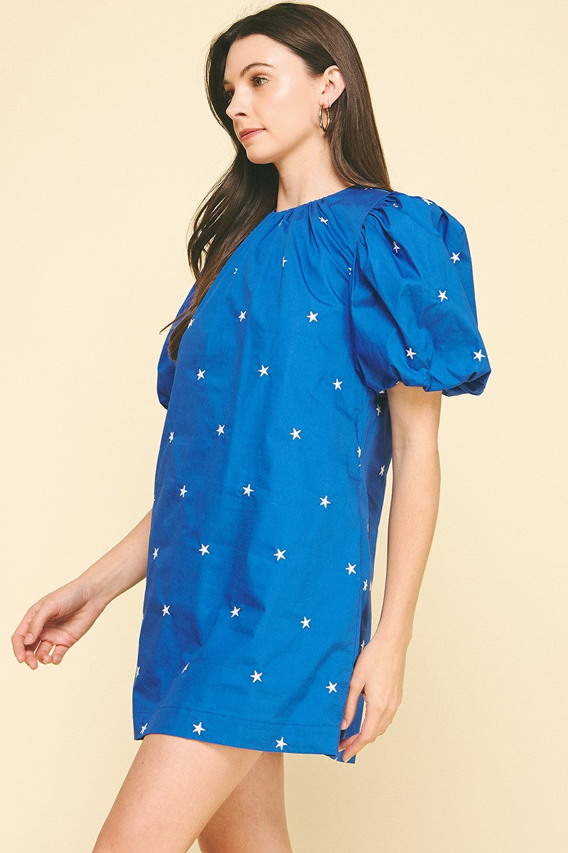 Woman wearing a blue Miggy Star Embroidered Mini Dress with white star patterns and puff sleeves.