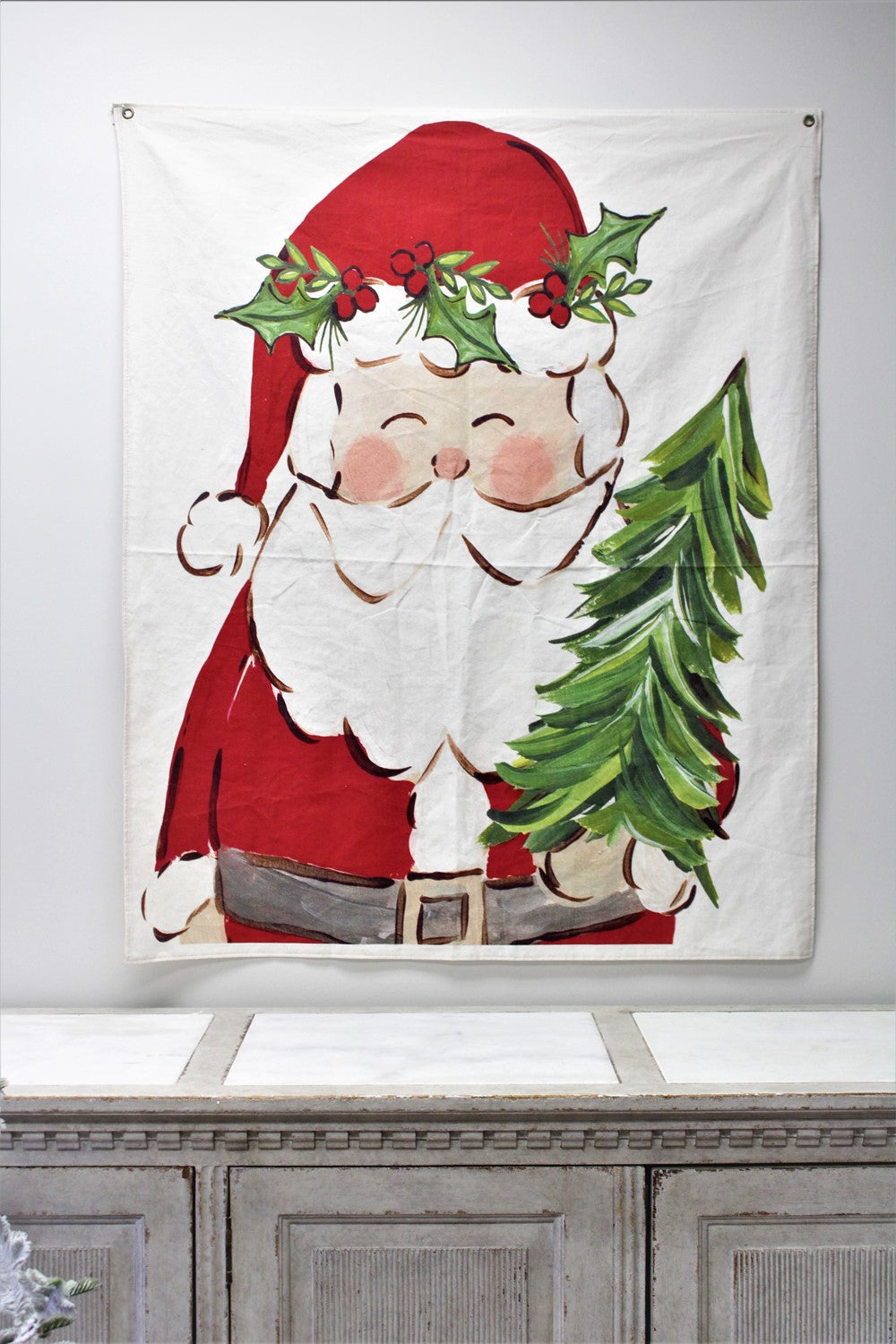 Fabric wall hanging featuring a painted Santa Claus with a holly crown holding a small green tree.
