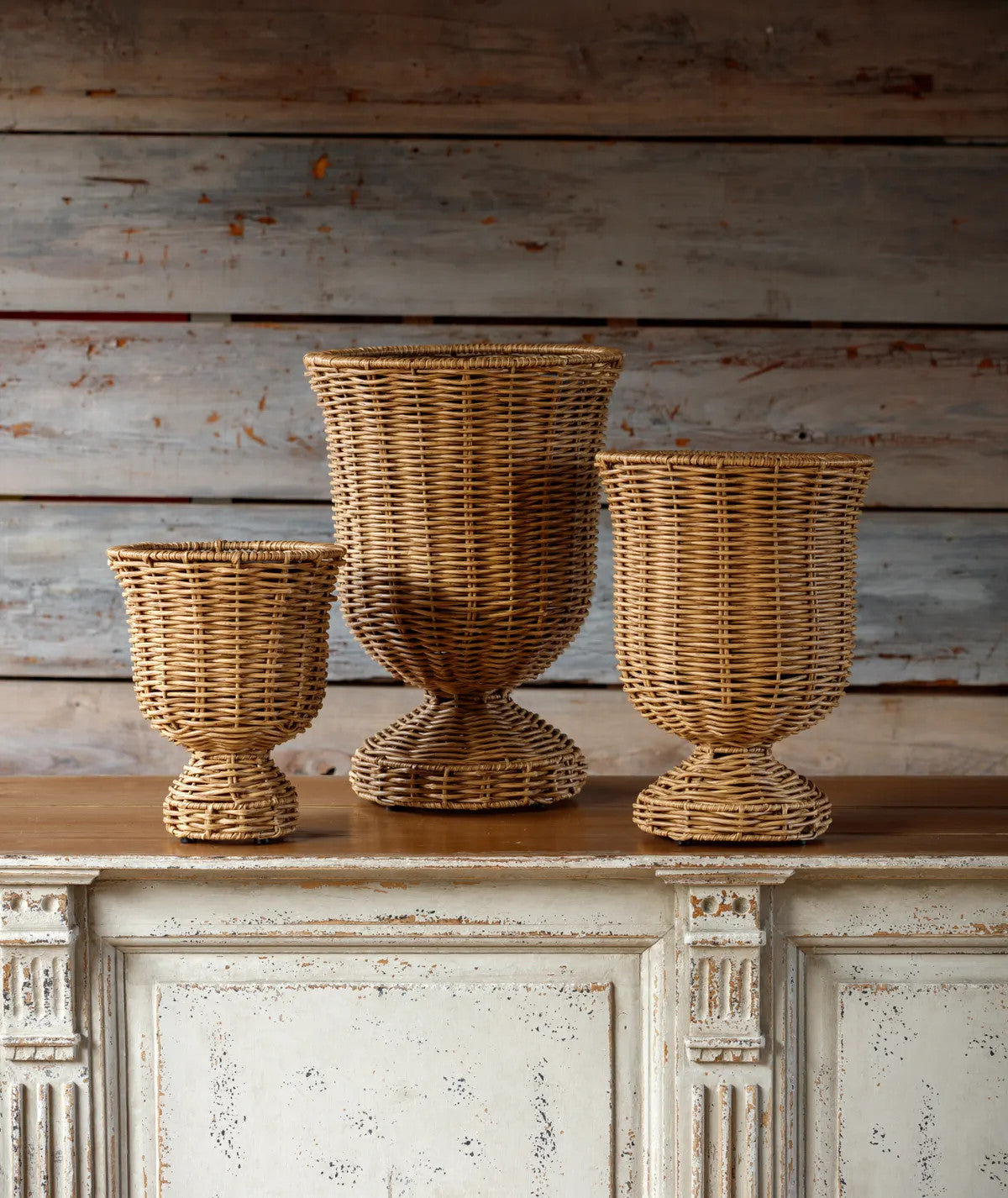 Three woven urns of varying sizes in natural wicker, each with a pedestal base.