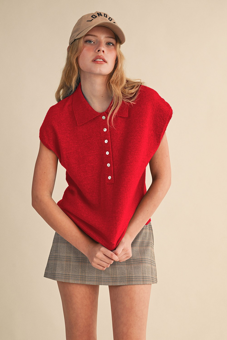 Woman wearing a red Jean cap sleeve collared sweater vest with a plaid skirt and tan baseball cap.