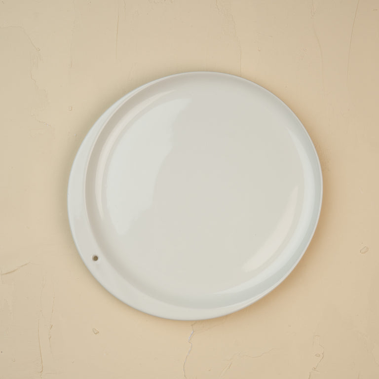Top-down view of a minimalist white ceramic Celebration Circle plate with a single small hole.