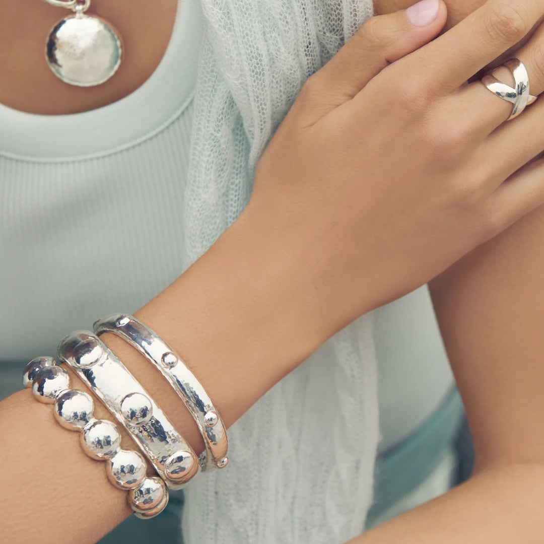 A person wearing the silver Solara Bangle stacked with other silver bracelets and a ring.
